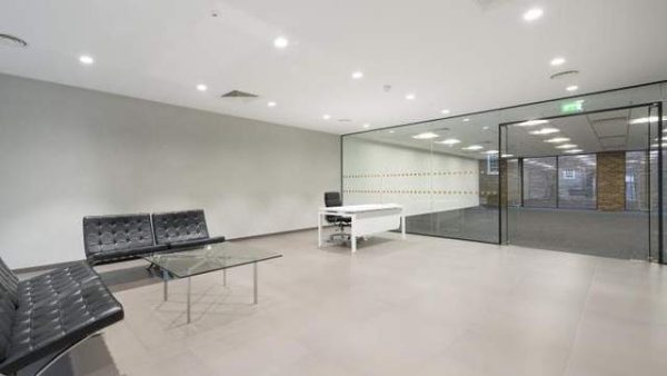 stylish pinned leather sofa chairs in a waiting area with glass coffee table and glass wall entrance to the office space