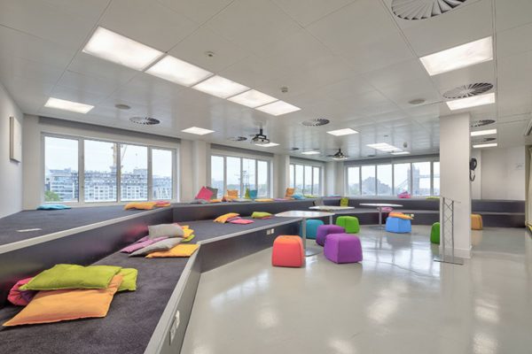 funky coloured stools around tables and floor cushions dotted about a carpeted space with views of Tower Bridge