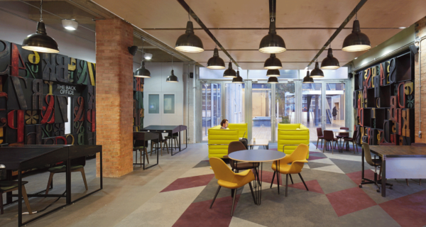 trendy break out space with desks, tables and chairs, shapes in the carpet, brick pillars and black walls covered in big colourful stencilled letters