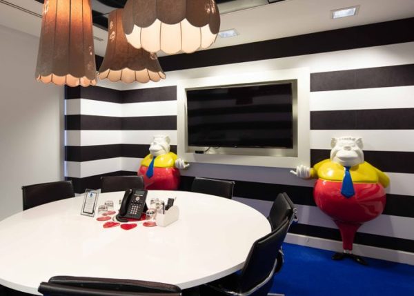 alt="tweedle dum and tweedle dee holding screen in a meeting room with black and white striped wall, round table and chairs and phone"