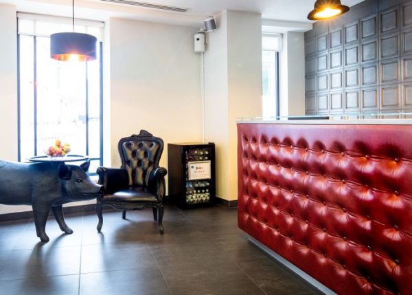 reception waiting area with pinned leather upholstery, drinks fridge and table shaped like a pig carrying a tray of apples