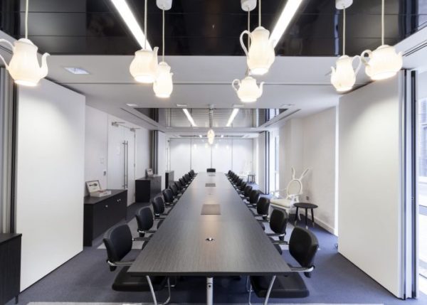 meeting or conference room with long table and chairs either side with hanging glowing teapot lamps and a white rabbit themed chair to one side