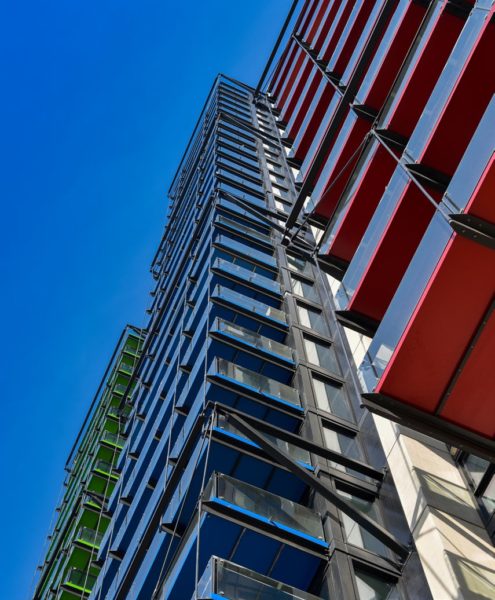 angled view looking up at modern building front on the Albert Embankment with green, blue and red balcony bottoms, and a blue sky