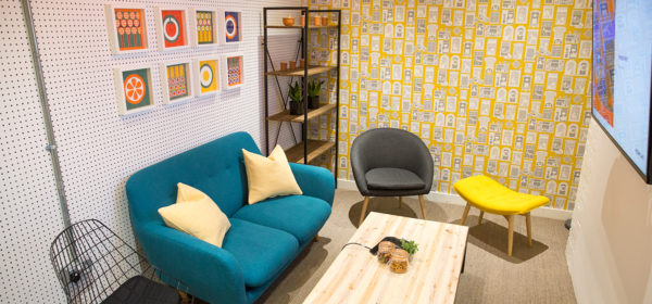 retro meeting room with colourful patterned wallpaper and funky furniture, jars of sweets and pretzels on the table and plants on shelves